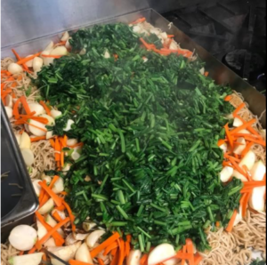 An image of Tokyo turnip yakisoba, a pile of greens with carrots and potatoes on top of noodles