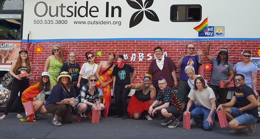 Large group of staff standing in front of Outside In medical van, staff are dressed to participate in the annual Pride parade