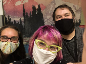 Three humans wearing masks and "smiling" with their eyes